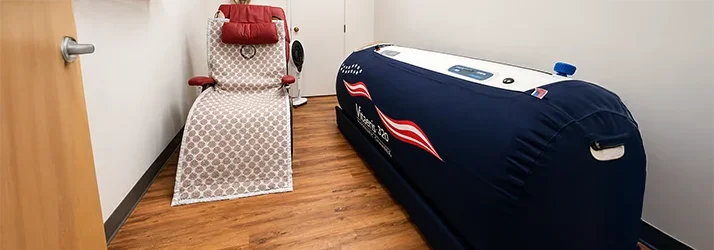 Room with a large blue chamber, a reclining chair with a red cushion, and wood flooring.