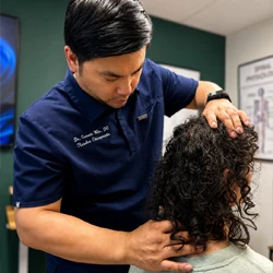 Practitioner performing a manual neck assessment on a seated patient in a clinical treatment room.