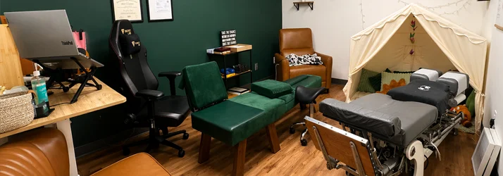 Treatment room with adjustment table, workstation, chairs, shelving, and a small tent-style play area.