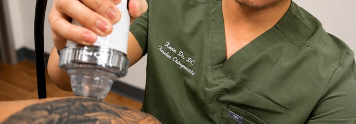 Close-up of a practitioner using a handheld therapy device on a patient's upper back during treatment.