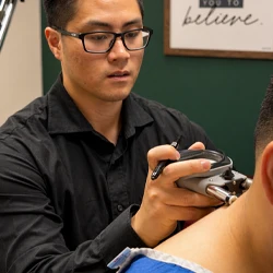 Practitioner using a handheld instrument on a seated patient's neck during an examination.